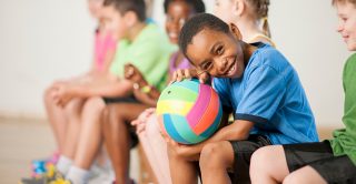 Child sits with a football in PE class