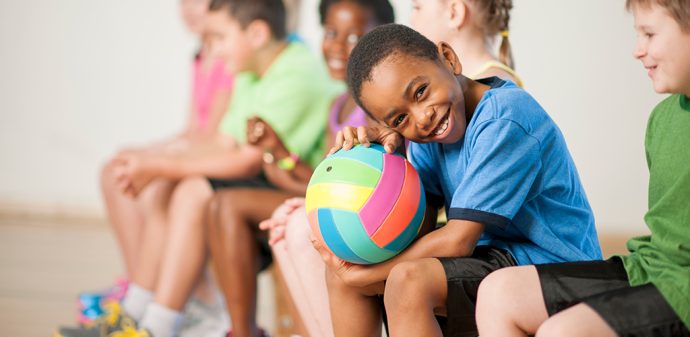 Child sits with a football in PE class