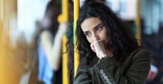 Thoughtful looking woman leans against a pole on public transport