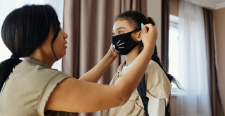 a mother helps her young daughter put on a face mask